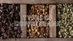 wooden tray with different colored coffee beans with text overlay "types of coffee beans"