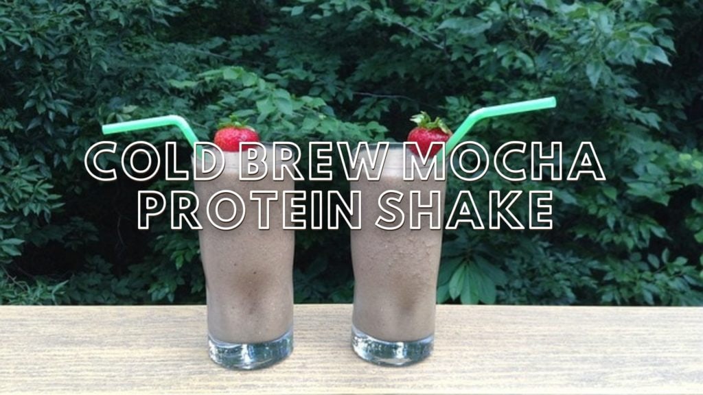 two mocha protein shakes on a table outside with trees in the background. Text overlay "cold brew mocha protein shake"