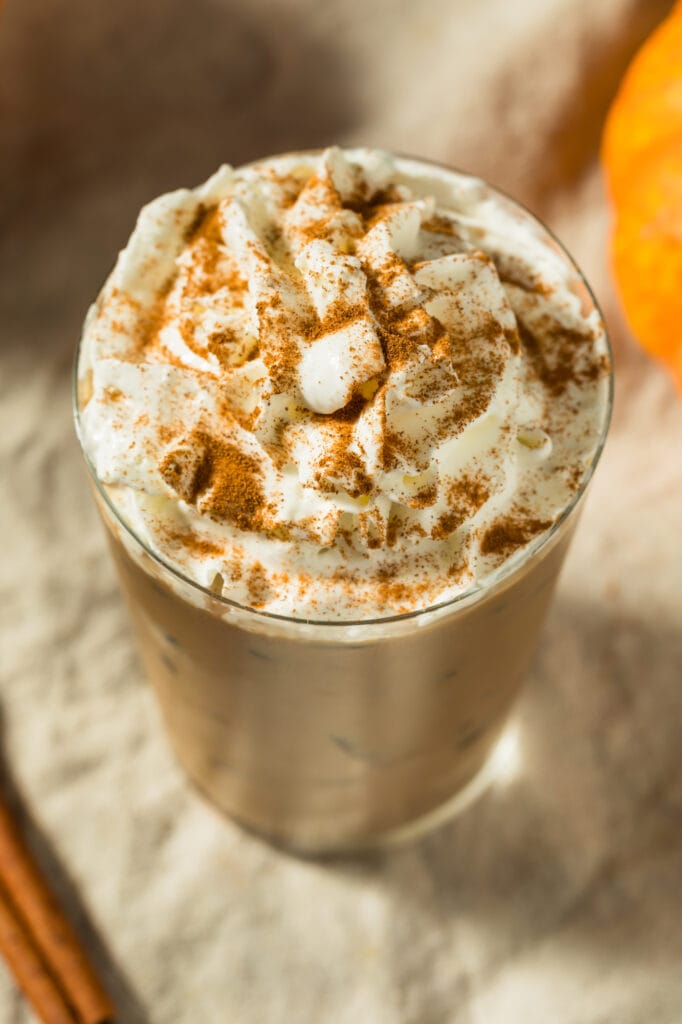 A pumpkin spice latte with whipped cream and cinnamon sticks on a beige napkin, overhead view